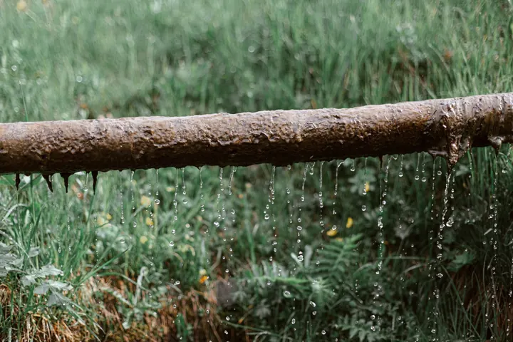 Rusted pipe dripping water over a lawn